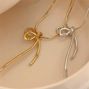 Gold and silver bow pendant snake chain necklaces with zircon in a ceramic dish