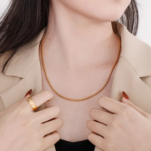 Close-up of golden stainless steel chain necklace worn on model with matching ring