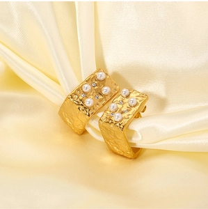 Macro shot of 18K gold plated wide square earrings with small pearls on beige satin cloth