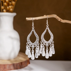 Close-up of bohemian hollow teardrop earrings with silver leaf tassel charms on wood