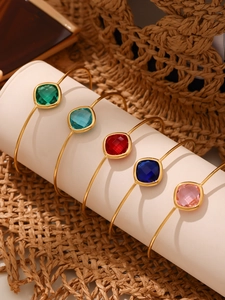 Detail view of five gold-plated open bangles with colorful square-cut gemstones