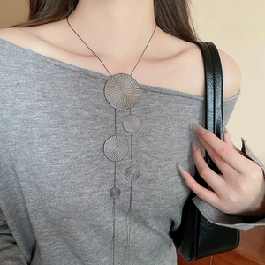 Detailed close-up of geometric circular metal discs with spiral texture on a long sweater chain