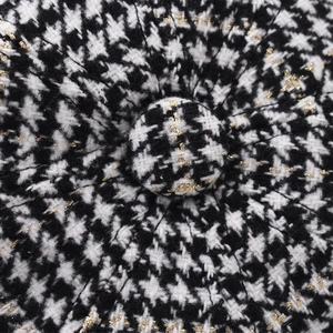 Close-up of black and white houndstooth fabric with gold metallic thread and fabric button