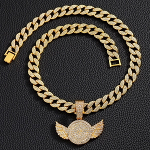 Close-up of golden iced out wing pendant and sparkling Cuban link chain on leather
