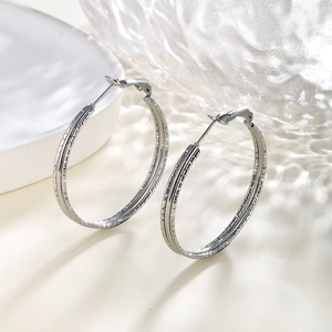 Detailed view of silver hoop earrings with textured chain patterns on a neutral surface