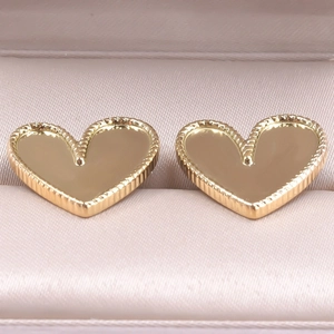 Macro shot of gold heart earrings with mirror finish and rope texture on pink silk