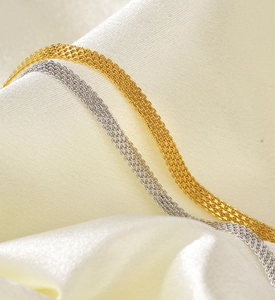 Macro detail of gold and silver woven mesh chains on elegant white silk fabric