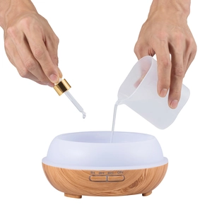 Detail showing essential oil being added with a dropper to the wood grain aroma diffuser