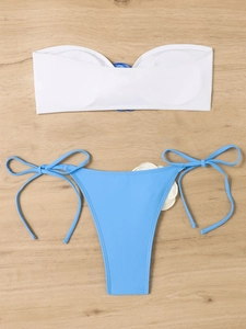 Flat lay of a two-piece bikini set with white bandeau top and blue side-tie bottoms on wood