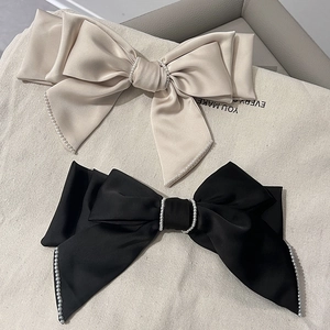 Detail of elegant satin bow hair clips with white pearl trim in black and champagne