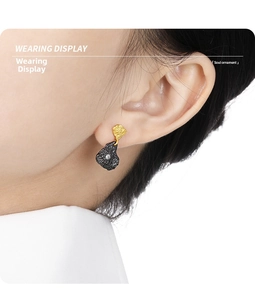 Close-up of irregular black and gold rock earrings with sparkling zircon on a model's ear