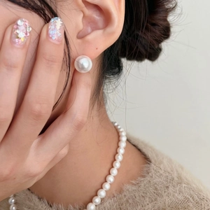 Close-up of 12mm white pearl earrings and necklace on a model wearing knitwear