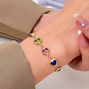 Close-up of heart-shaped faceted gems in green and pink on a gold chain necklace