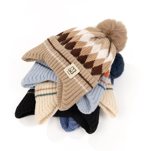 Close-up of thick knitted baby beanies with earflaps, pom-poms and leather M labels