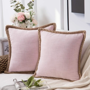 Set of two pink linen throw pillow covers with jute fringe trim on a cozy sofa