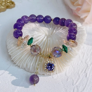 Detail of amethyst beaded bracelet with zircon-set flower pendant on white coral base