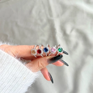 Close-up of five S925 silver halo rings with colorful square zircon stones on a soft fabric