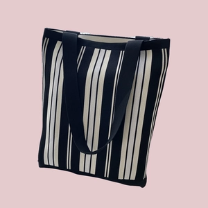 Detail of the black and white striped knit tote bag with black handles on pink background