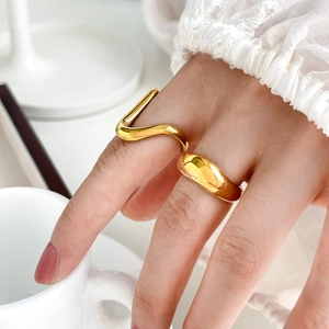 Detailed close-up of golden wavy curve ring and thick smooth round band on model hand