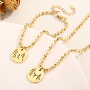Detailed view of two gold family necklaces with a parents and child pendant on a display stand