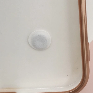 Close-up of a white protective felt pad with adhesive backing on a phone case surface
