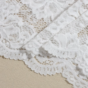 Close-up of white lace dress fabric with delicate floral patterns and scalloped edges