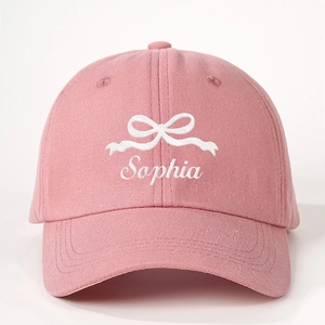 Détail de la casquette rose avec icône de nœud blanc et broderie Sophia élégante