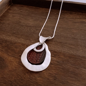 Close-up of vintage silver droplet pendant with brown woven texture on a wooden tray
