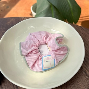 Detail of pink striped scrunchie with green trim and NOTES label on ceramic dish