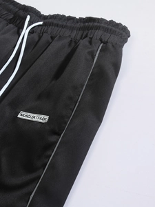 Detail view of woven joggers featuring an elastic waist with white drawstrings and logo