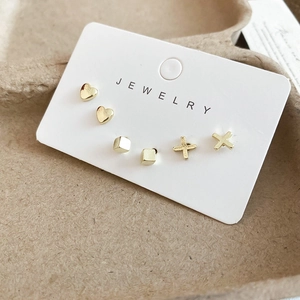 Detailed close-up of gold heart, square and cross stud earrings set on a jewelry card