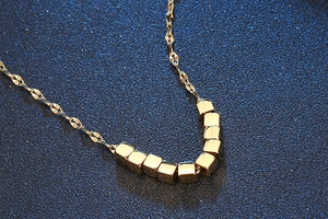 Detailed shot of polished gold titanium necklace with minimalist cube pendants on blue