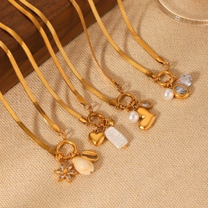 Macro detail of four gold snake chains with pearl and heart pendants on fabric
