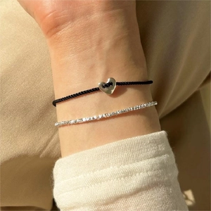 Detail of layered S925 silver beaded bracelet and black cord with silver heart charm