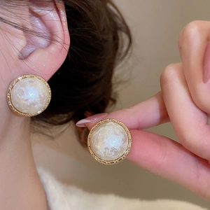 Detail view of pearl earrings with textured gold frame and marble inlay on ear