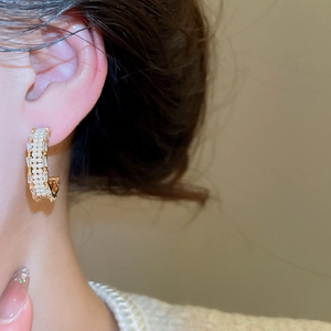Close-up of gold-plated C-shape earrings with pearls and zircon on model side view