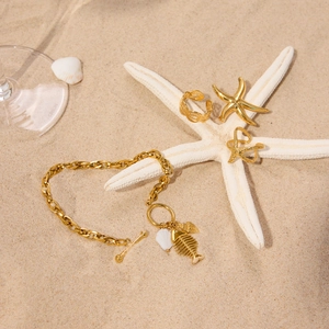 Gold beach jewelry set featuring shell pendant bracelet and starfish rings on white sand