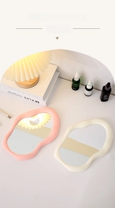 Close-up of pink and cream irregular wavy cloud-shaped desktop mirrors in warm lighting