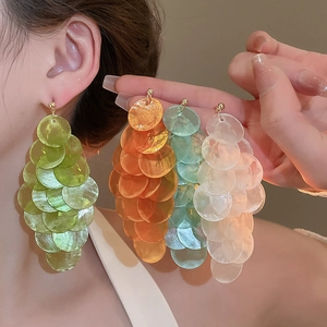 Detail view of long tassel shell earrings in green and orange tones on model's ear