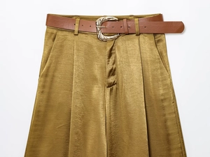 Detail of satin mustard pants with a brown belt and wavy golden metal buckle