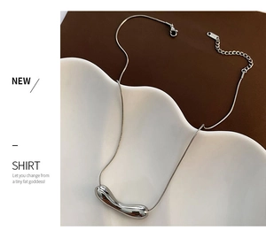 Close-up of polished silver snake chain with an irregular bean-shaped pendant on a tray