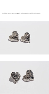 Detailed close-up of silver heart stud earrings with lava texture and zircon center