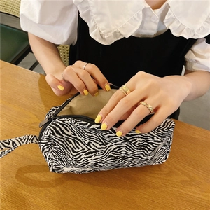 Détail d'une trousse de maquillage zébrée avec poignée et fermeture sur table bois