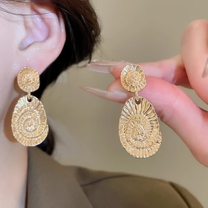 Close-up of gold oval drop earrings featuring intricate radiant swirl textures