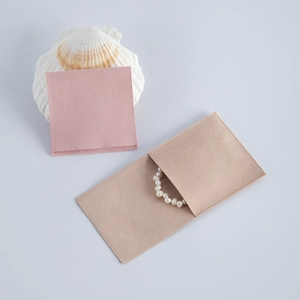 Pink and beige envelope suede jewelry pouches with a pearl bracelet on a grey background