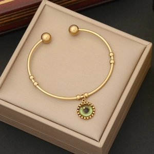 Bracciale rigido dorato evil eye con ciondolo verde su un cuscino beige per gioielli
