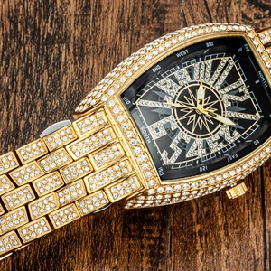Close-up of gold iced-out tonneau watch with compass dial on a wood surface
