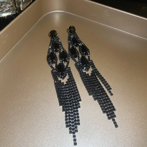 Macro shot of long black tassel earrings featuring multiple rhinestones on a gold tray