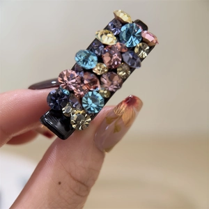 Gros plan d'une pince à cheveux noire avec des strass colorés dans une main