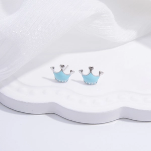 Macro view of silver crown earrings with light blue enamel finish on white tray